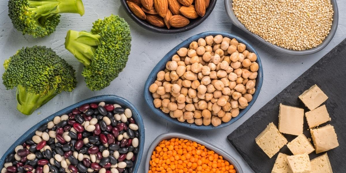 Raw vegan ingredients on a table top; broccoli, beans, lentils, almonds and grains.