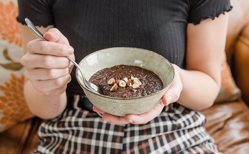 Person holding a breakfast bowl with Purition Chocolate that's been made into an instant porridge, sprinkled with extra hazelnuts.