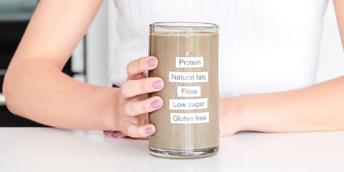 A full glass of Purition wholefood meal shake with labels up the front of the glass listing; Protein, Natural fats, Fibre, Low sugar, Gluten free.