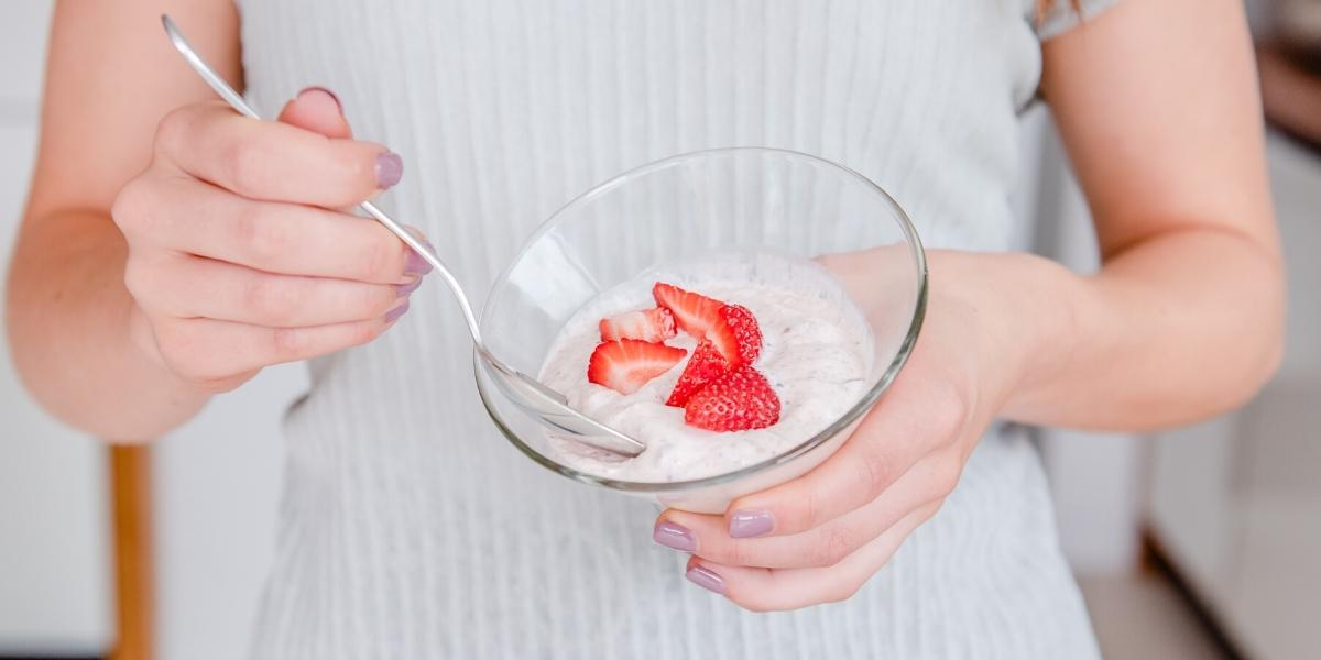 Person about to enjoy a Purition Strawberry yoghurt bowl topped with fresh strawberries.