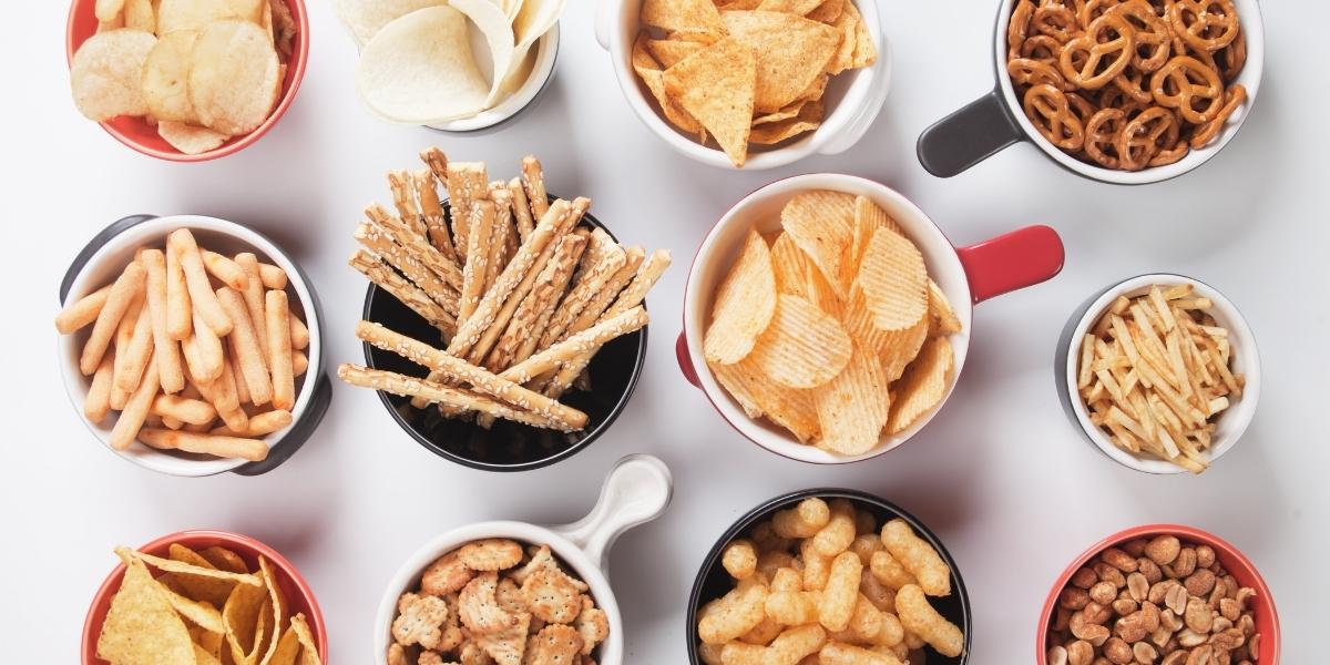 Snack table; bowls of carbs heavy snacks like crisps, pretzels, cheesy puffs, tortilla crisps, bread sticks.