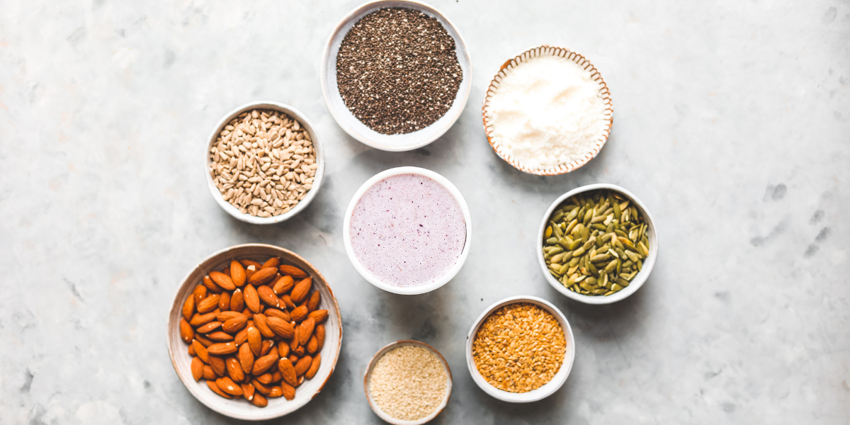 Pots of seeds and nuts with a Purition Blackcurrant smoothie in the middle.