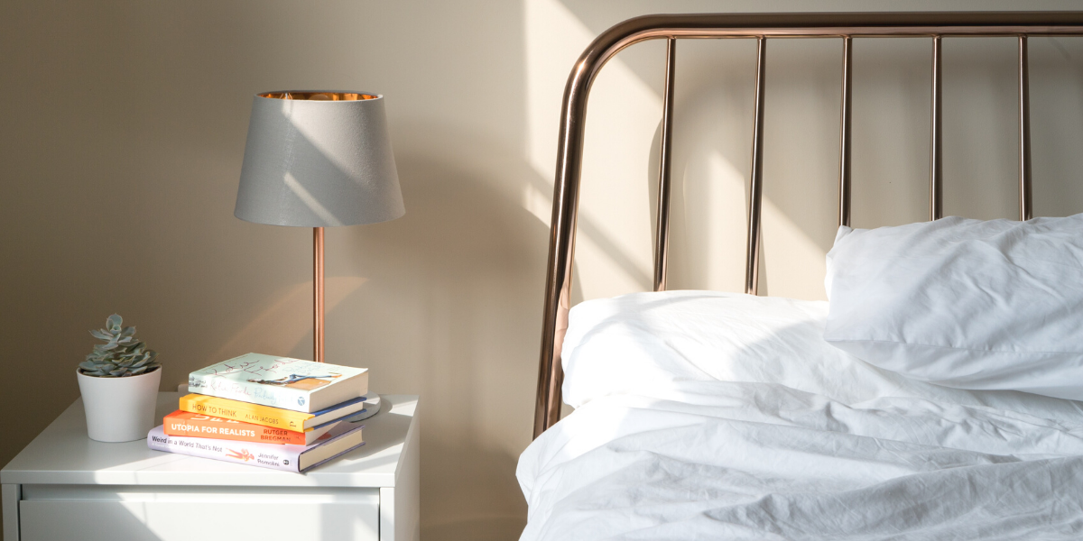 Bedside table with books and lamp, next to chrome bed frame with white sheets