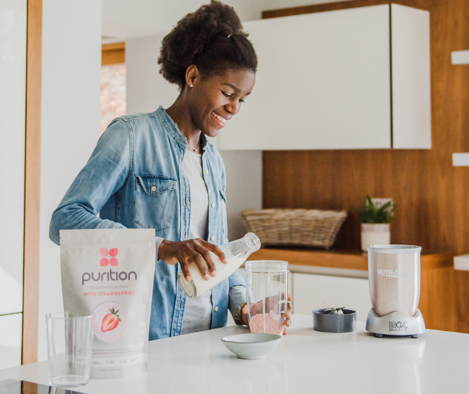 Woman pouring milk into blender cup whilst making a Purition Strawberry weight gain smoothie